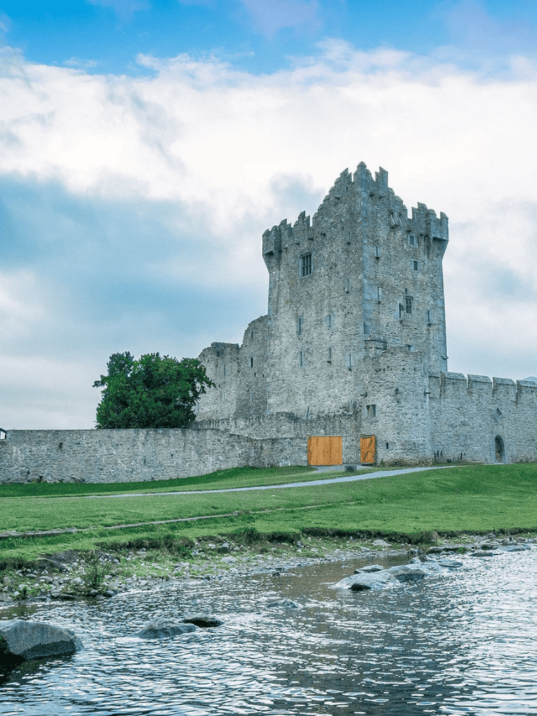 Medieval castle on riverbank with stone walls and towers, Scottish landscape, tourism, historical site.