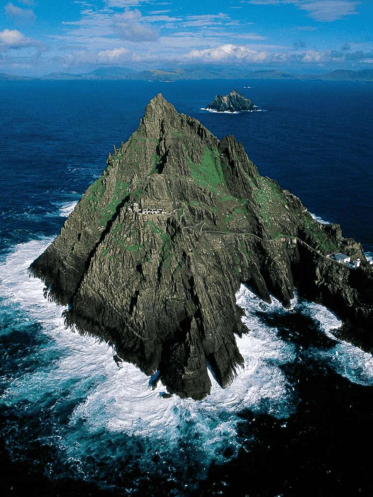 Majestic sea stack rock formation on rugged coast with lighthouse, dramatic ocean views.