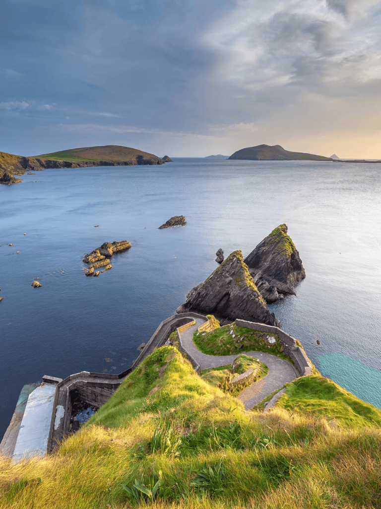 Cliffside coastal view with winding path and sea stacks at sunset, scenic travel destination.