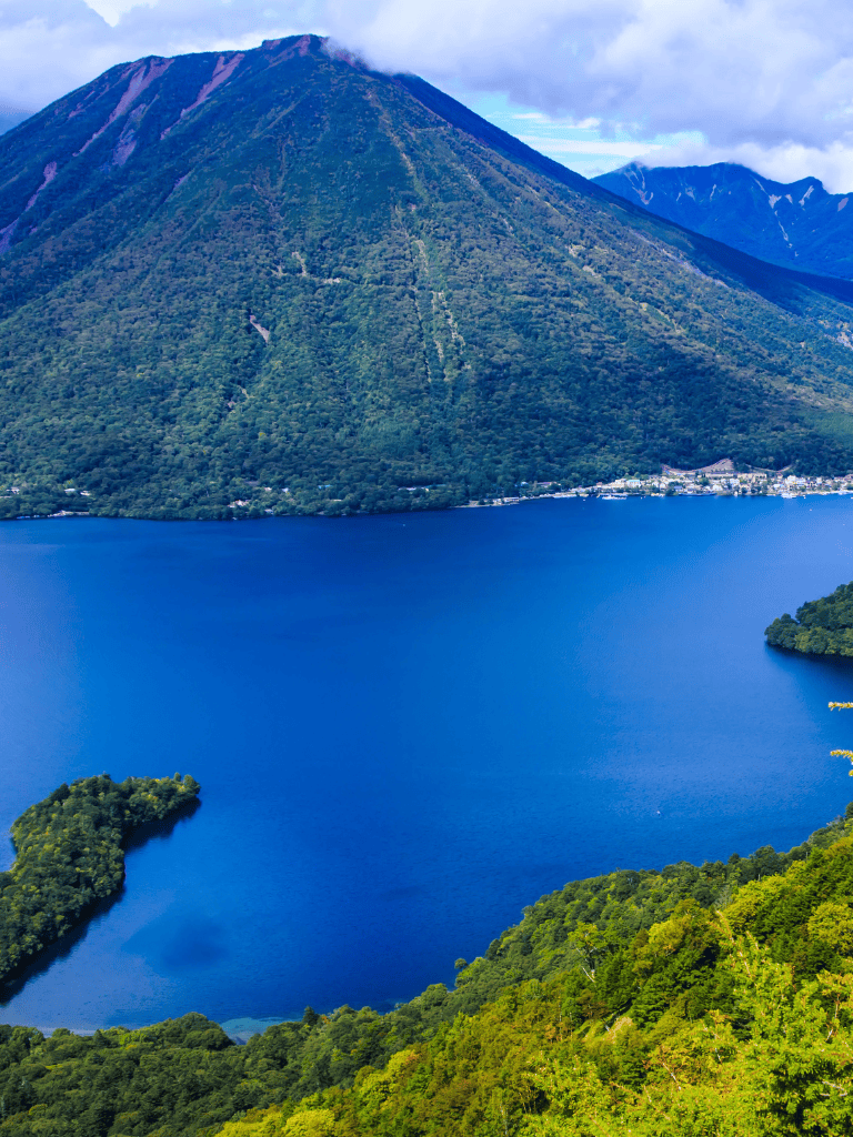 Serene lake with lush green mountains and volcanic peaks in the background, stunning natural landscape for outdoor adventures.