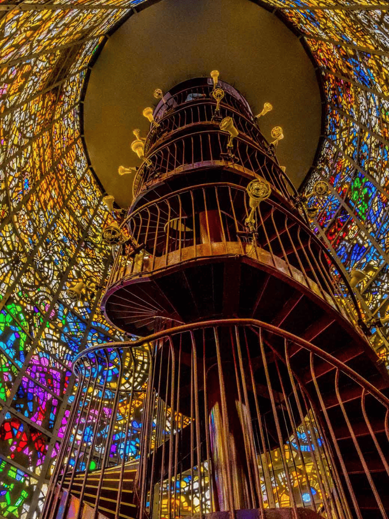 Colorful stained glass spiral staircase with artistic brass accents.