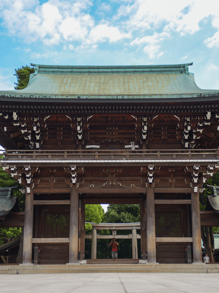 Intricate wooden temple gate in Japan, surrounded by lush greenery and blue sky.