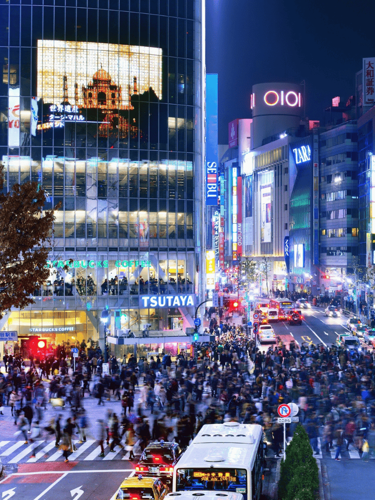 Vibrant Tokyo cityscape at night with bright neon signs, bustling crowds, and traffic intersection.