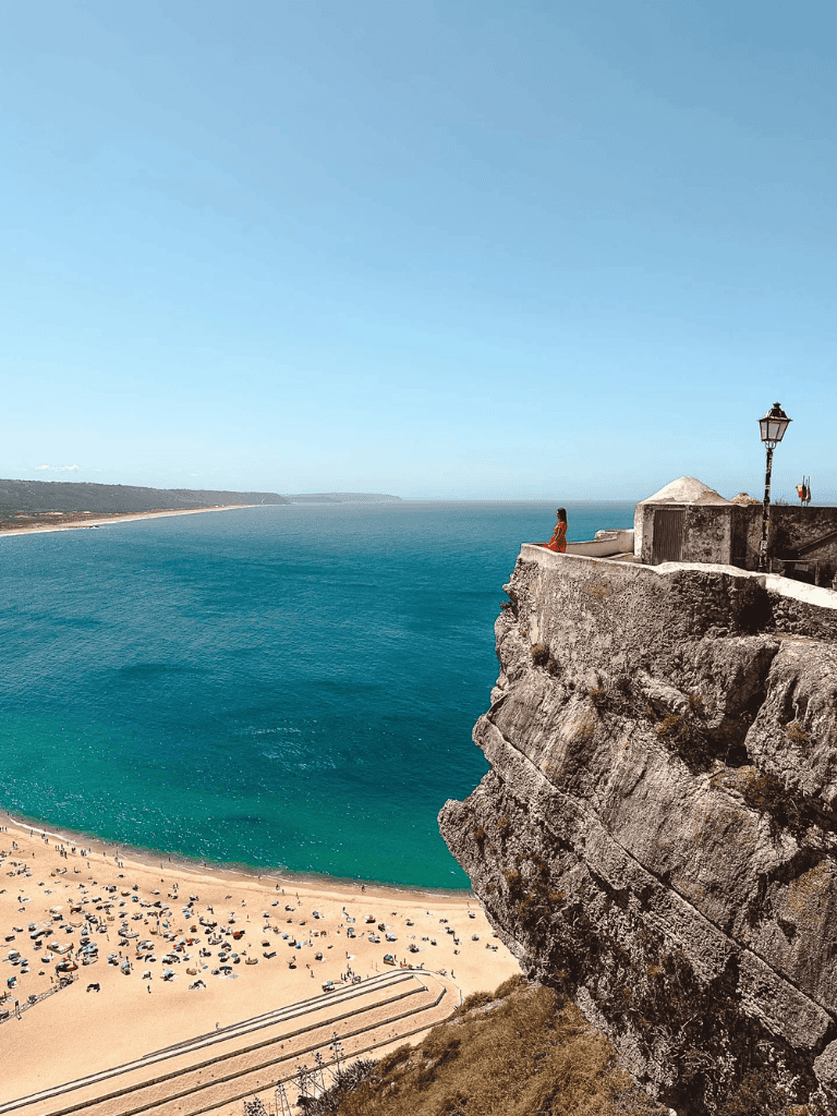 Breathtaking cliff overlooking a beach and ocean with a person gazing at the view.