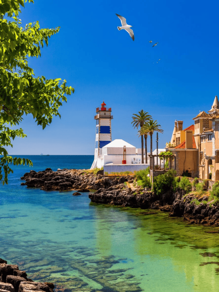 Seaside lighthouse with colorful buildings and palm trees, coastal scenery, and ocean view.