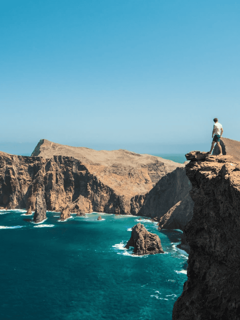 Breathtaking coastal cliff view with a person overlooking rugged rocks and ocean waves.