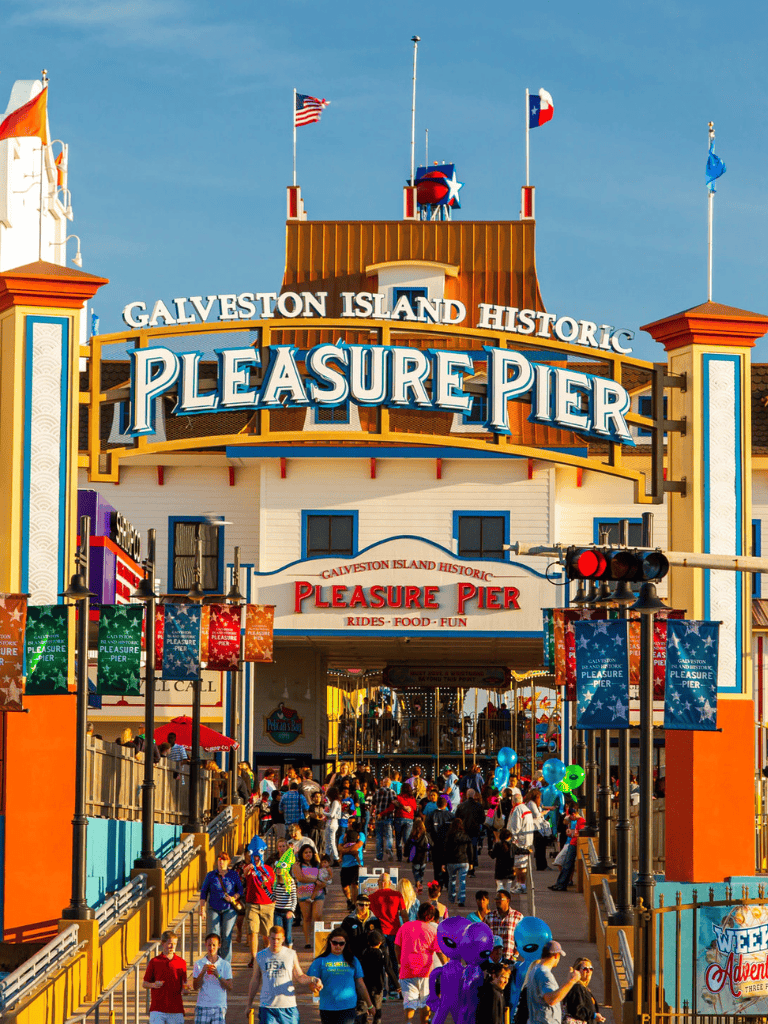 Galveston Island Pleasure Pier amusement park in Texas, lively crowd, colorful rides, iconic landmark, family fun destination.