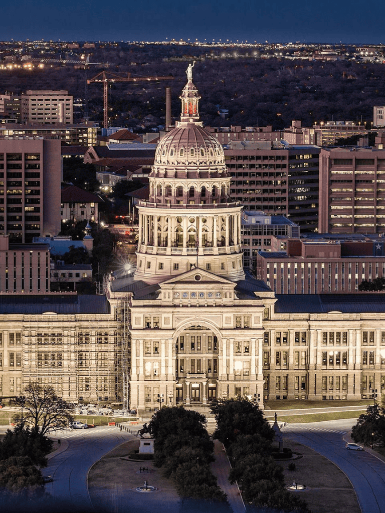 Historic Texas State Capitol building in Austin at dusk with cityscape background.