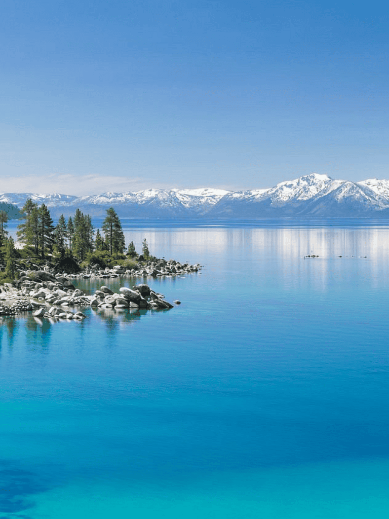 Serene mountain lake with snow-capped peaks and lush pine trees, perfect for outdoor adventures and scenic views.