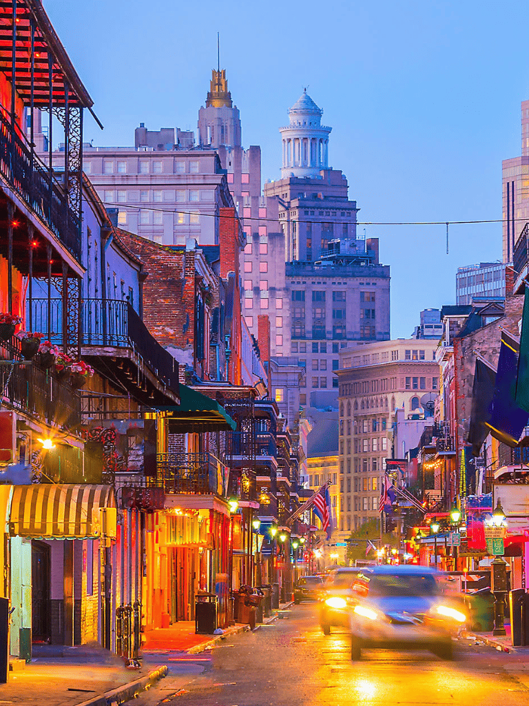 Vibrant city street at dusk with historic buildings and colorful storefronts, downtown skyscrapers in the background.