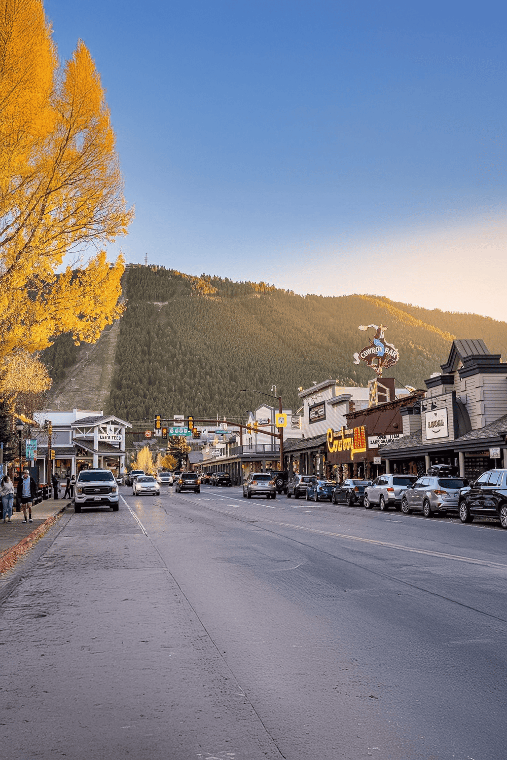 Charming mountain town street with local shops, trees, and mountain views, ideal for vacation planning and directions.