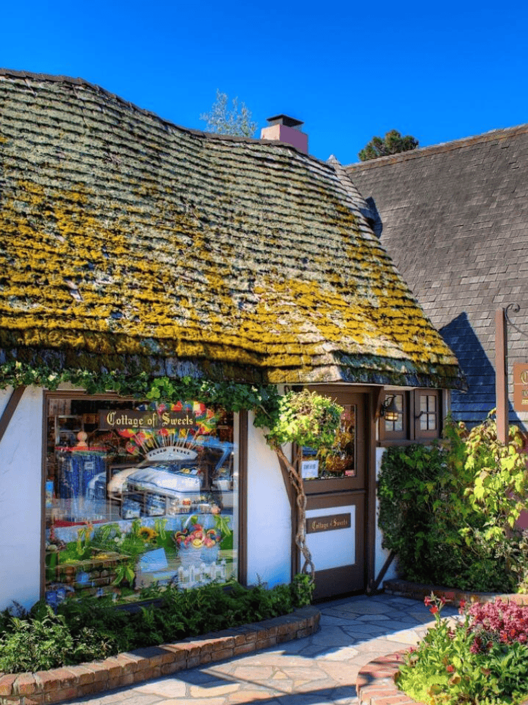 Colorful cottage bakery decorated with flowers, moss-covered roof, and cozy entrance.