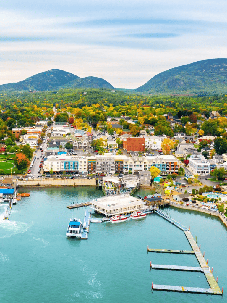 Charming waterfront town with colorful buildings, boats, and scenic mountain views in autumn.