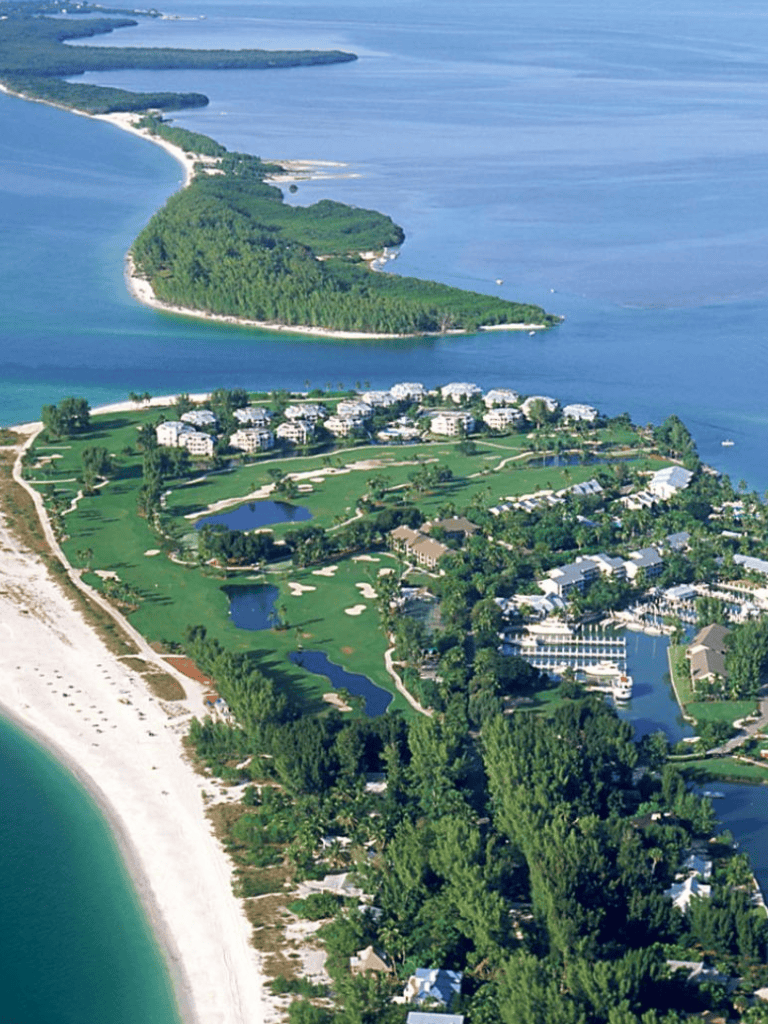Aerial view of a coastal resort with lush green golf courses, sandy beaches, and clear blue waters, emphasizing vacation travel and leisure.