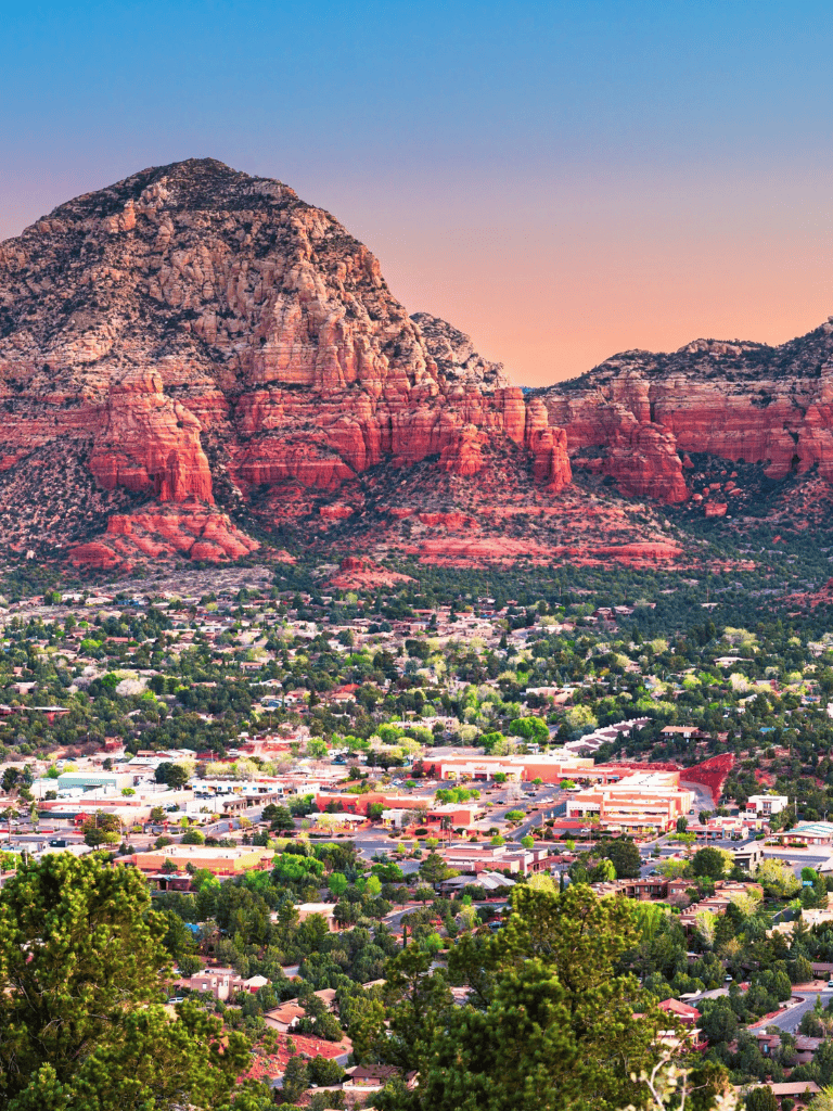 Vibrant sunset over Sedona's red rock formations and suburban landscape, showcasing natural beauty and local scenery.