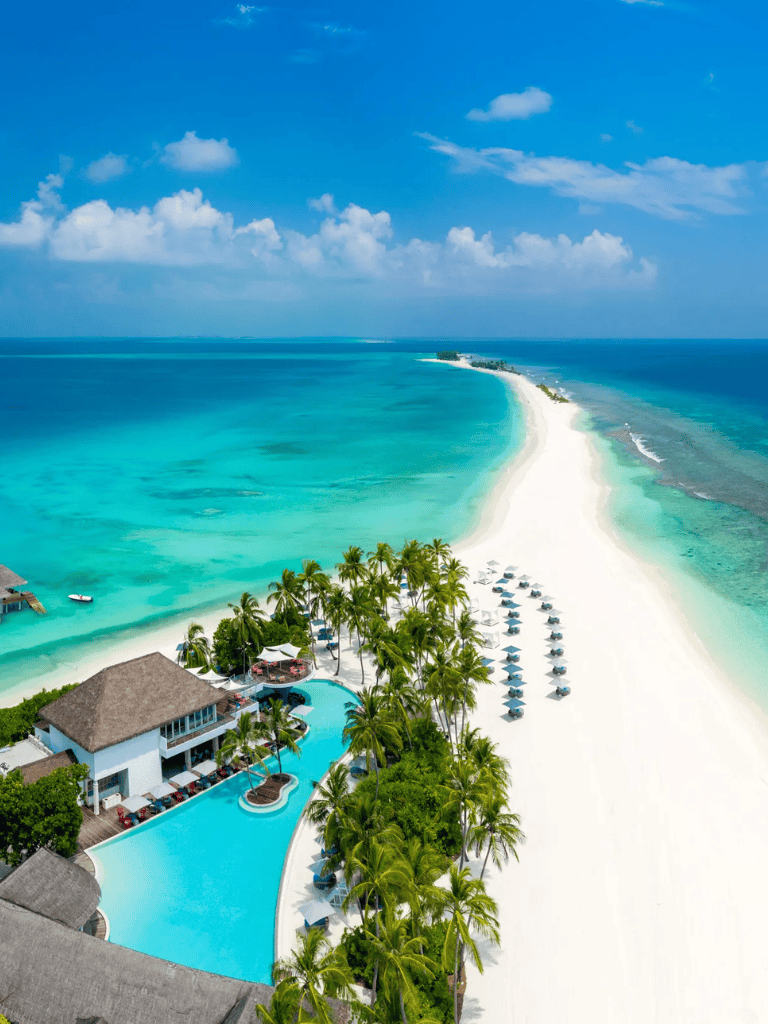 Luxurious beach resort with turquoise waters, white sand beach, and tropical palm trees.