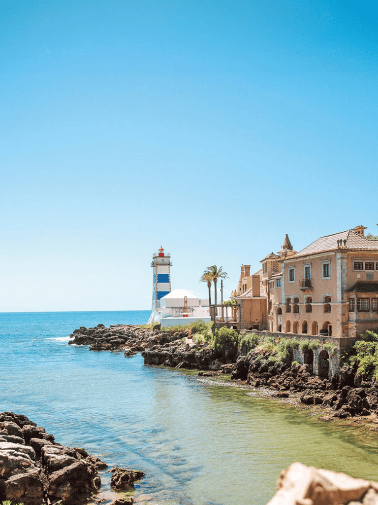 Lighthouse near coastal buildings, ocean view, Mediterranean seaside scene.