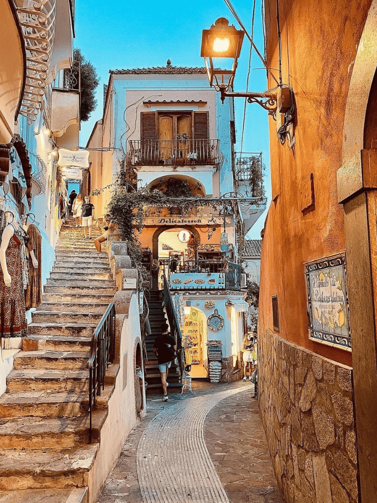 Charming narrow alley in Italy with vibrant architecture, stairs, and shops in a picturesque Mediterranean village.