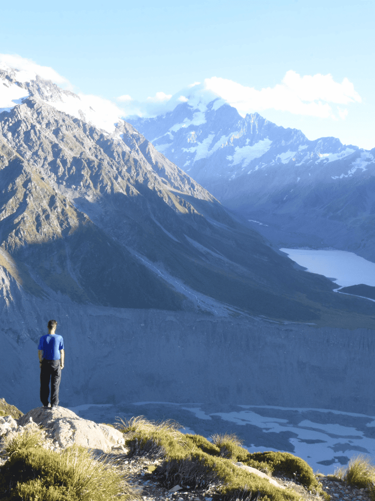 Majestic mountain landscape with a hiker overlooking snow-capped peaks and a serene lake, showcasing adventure and nature exploration.