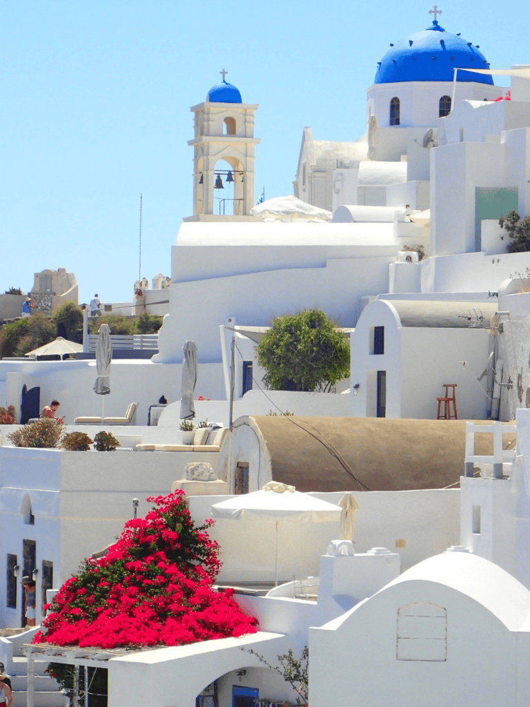 Picturesque Santorini white-washed buildings with blue domes and vibrant flowers, iconic Greek island scenery.