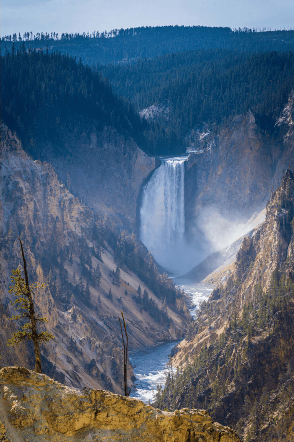 Vivid waterfall cascading into a deep canyon with dense forested mountains in the background.