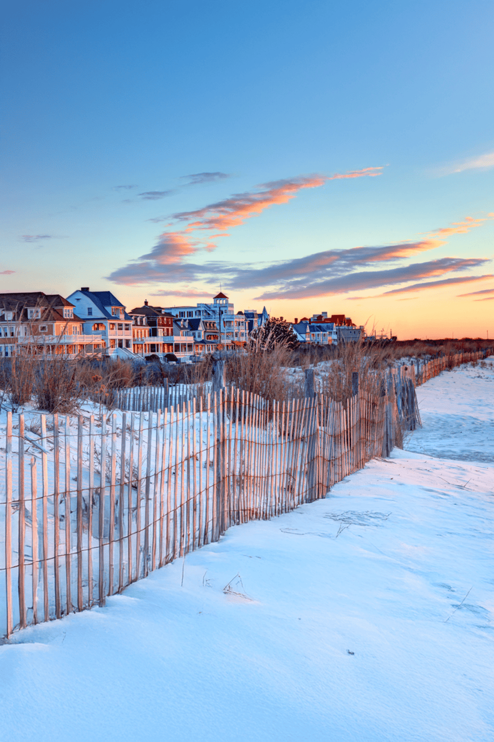 Colorful beach houses along a sandy shore at sunset with snow on the ground, representing coastal travel and scenic destinations.