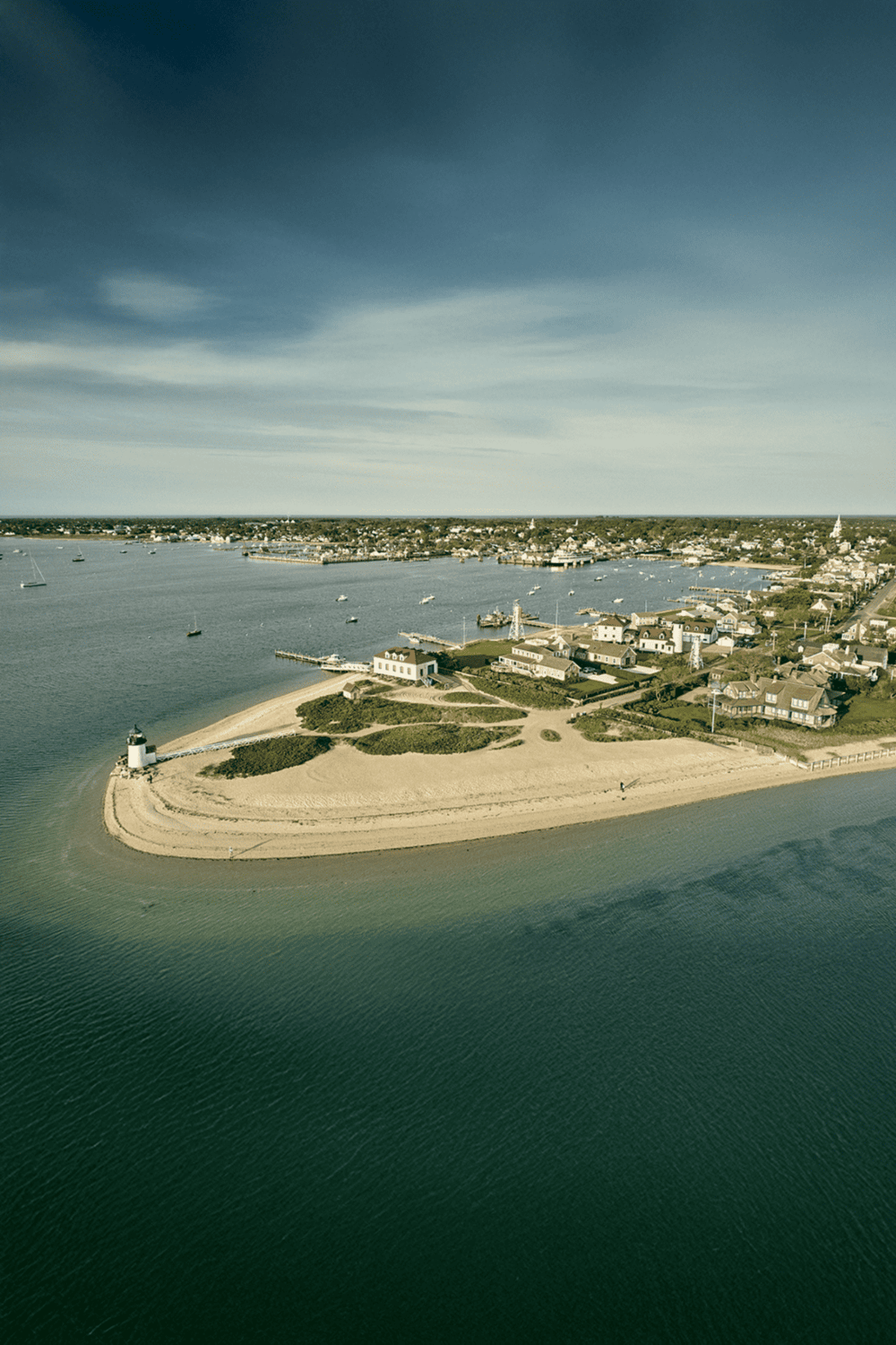 Aerial view of a coastal island with lighthouse, sandy beaches, and residential area, ideal for travel planning.