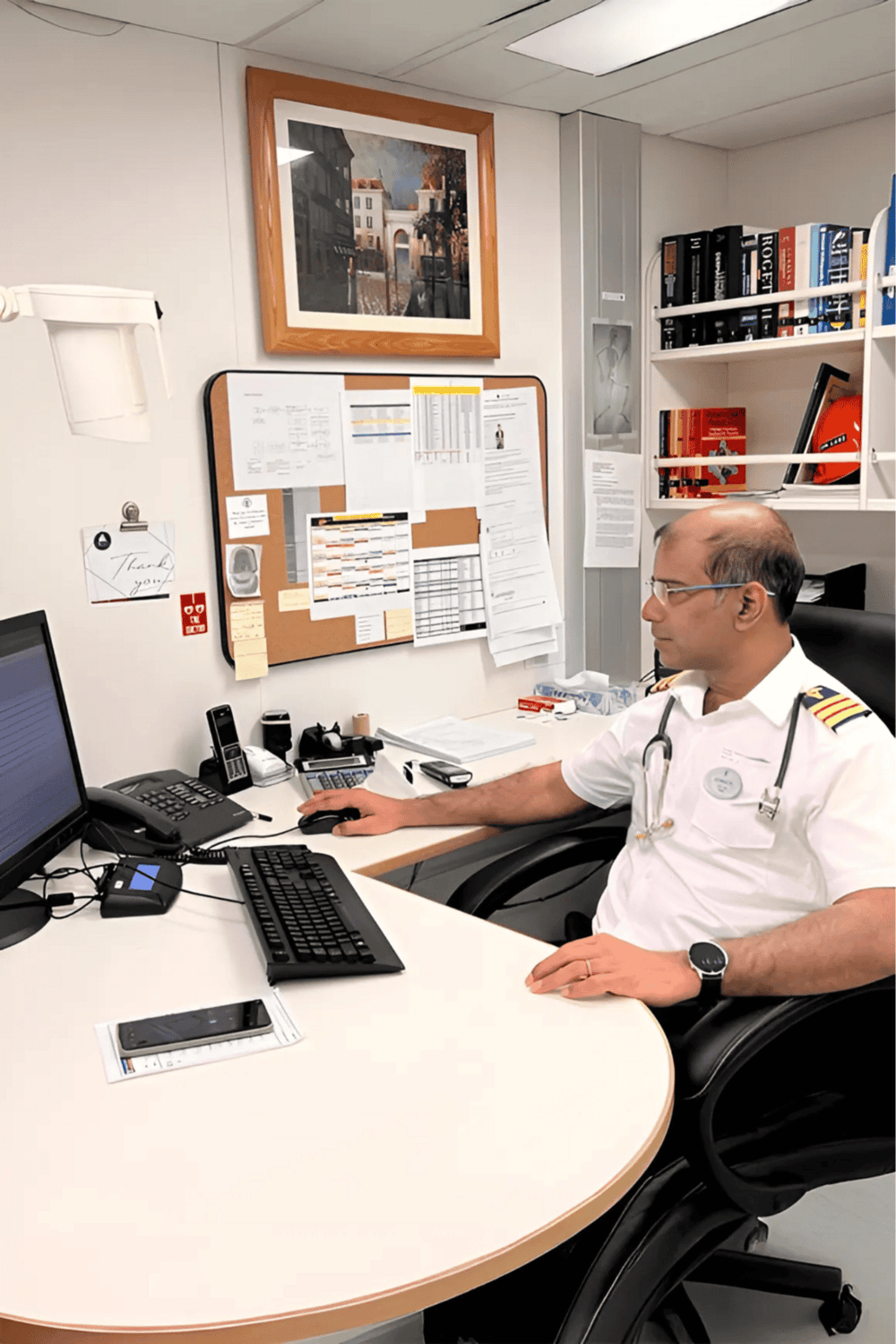 Emergency medical professional working at a desk with computer and medical supplies in an office setting.