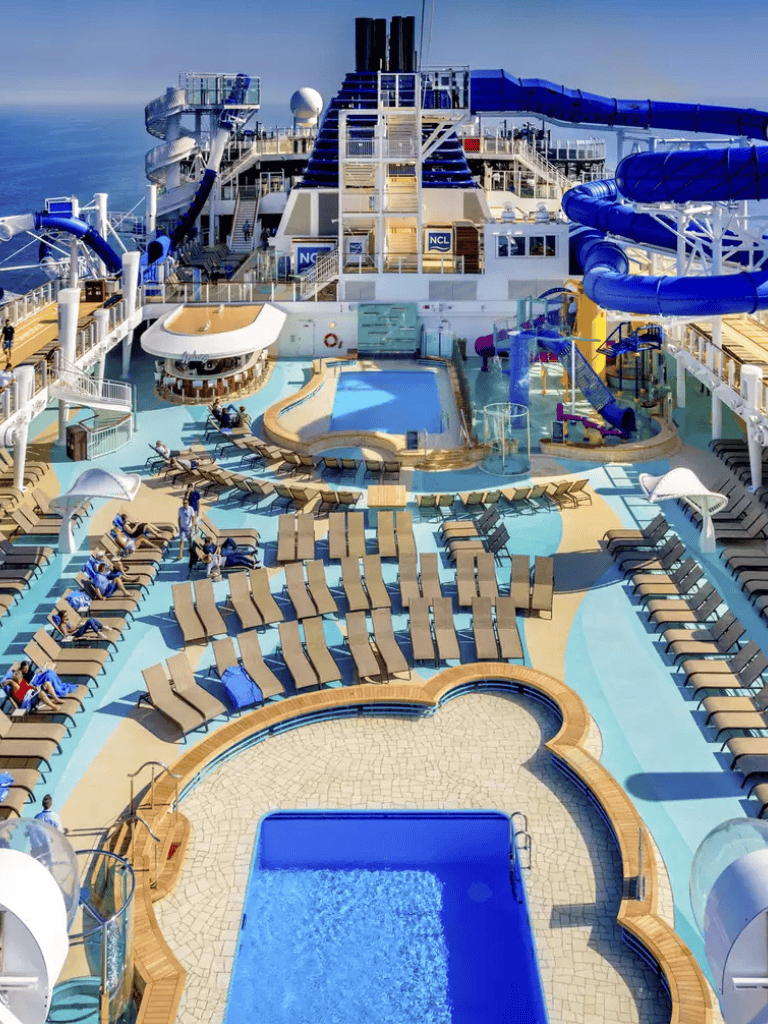Cruise ship's water slides and pool area on deck with lounge chairs and ocean view.