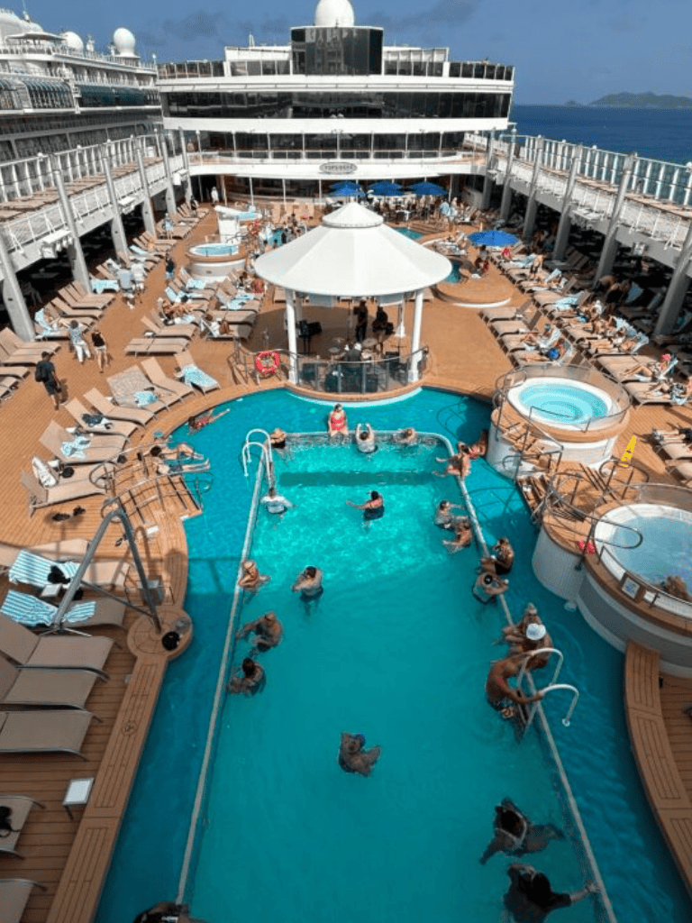 Kids and adults enjoying a pool on a cruise ship deck with loungers and hot tubs.