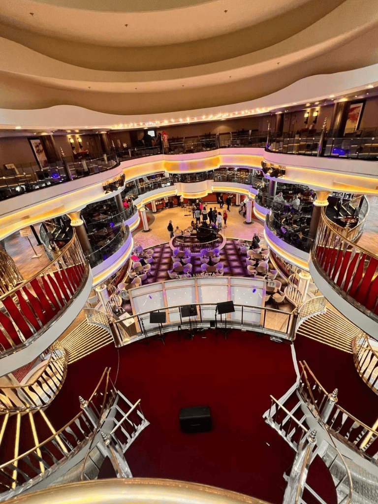Luxurious cruise ship interior with multi-level balconies, elegant lighting, and vibrant dining area.