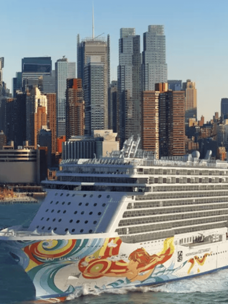 Cruise ship sailing in New York City harbor with city skyline in background.
