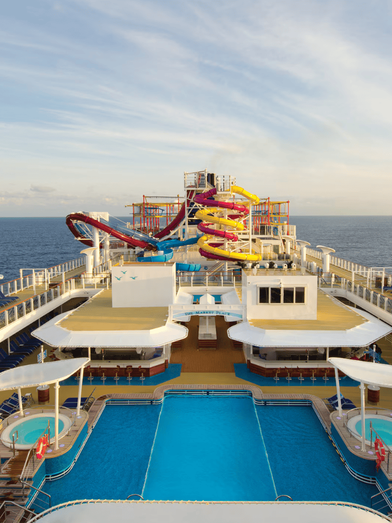 Colorful water slides on cruise ship deck with pool and ocean background.