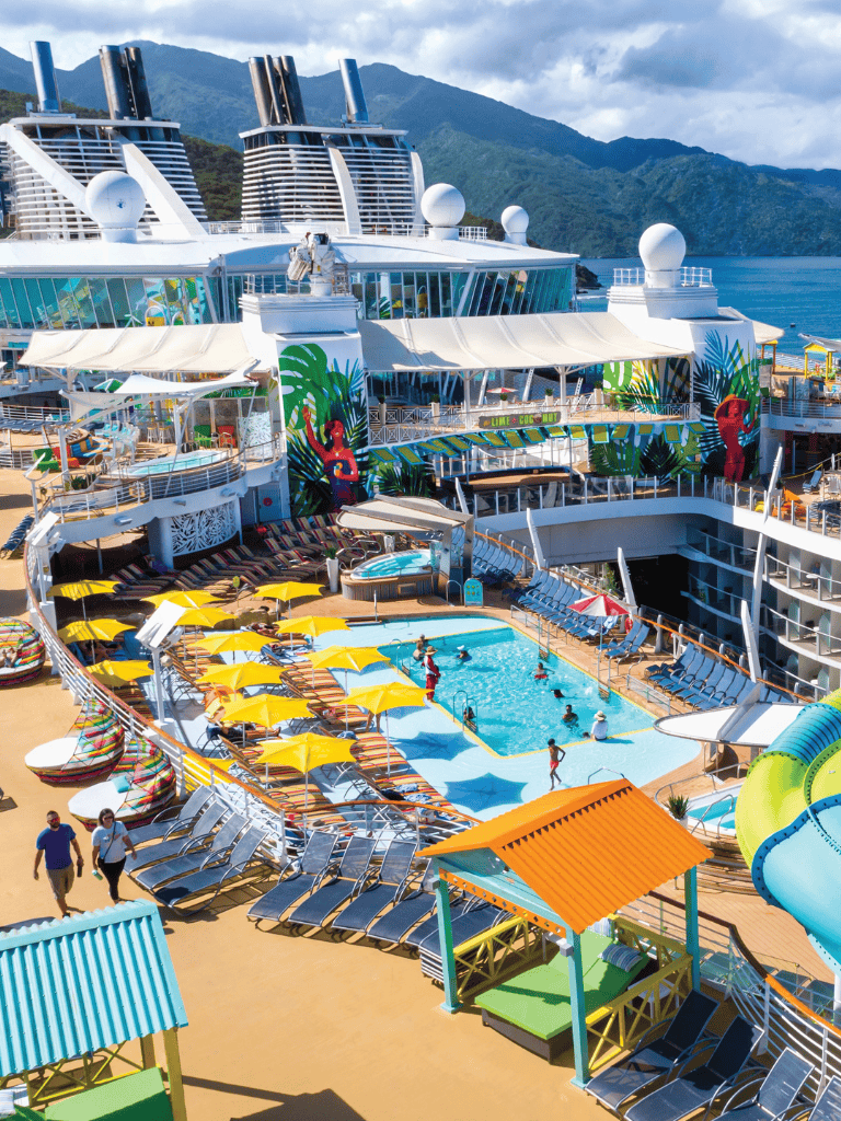 Luxurious cruise ship with swimming pool and water slides at sea, scenic mountain backdrop.
