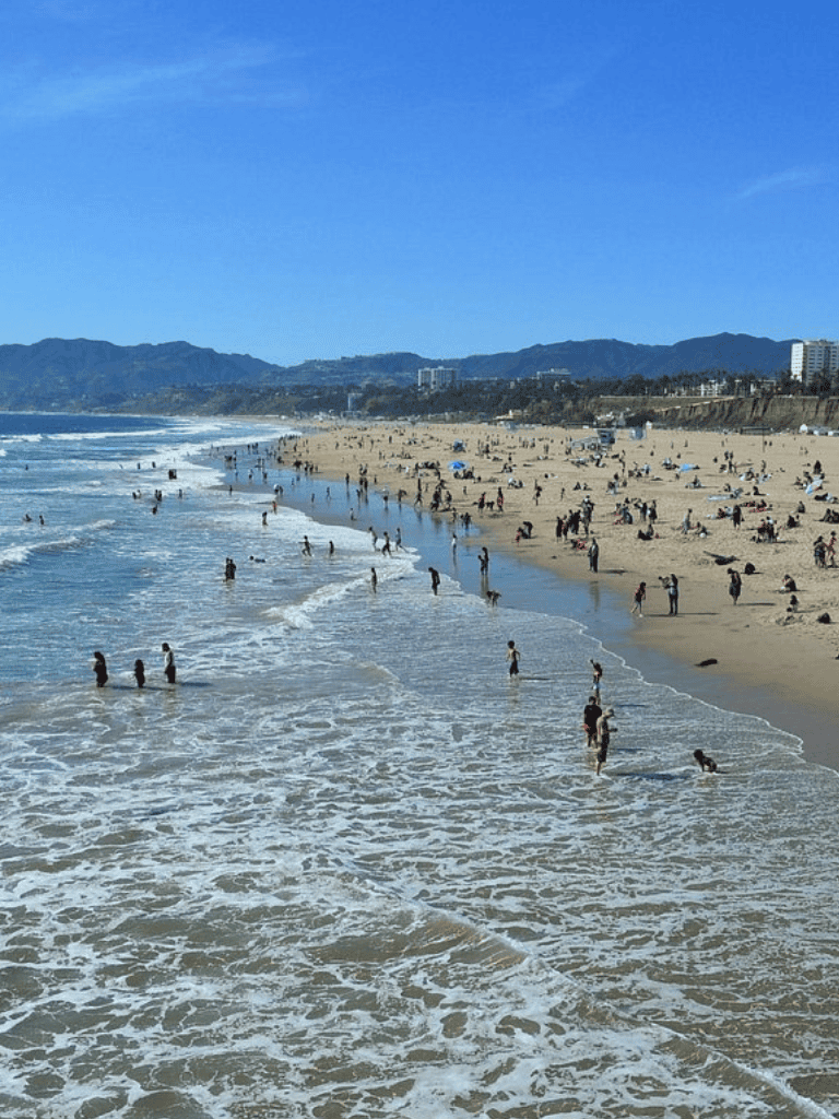 Busy beach with people swimming and relaxing on sunny coast.