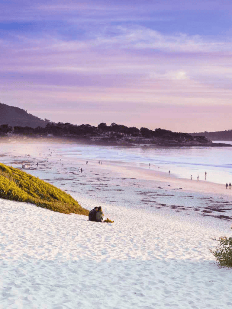 Serene beach landscape with sunset, people enjoying coastal scenery, ocean waves, and lush greenery.