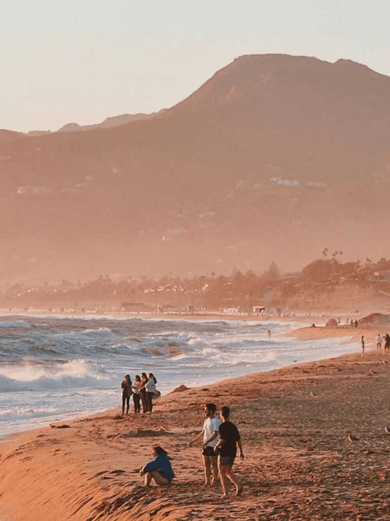 Beautiful sunset at the beach with people enjoying the ocean view and scenic mountain landscape in the background.