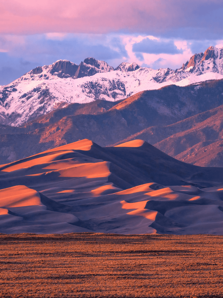 Snow-capped mountains and sand dunes at sunset, scenic desert landscape for travel and adventure tourism.