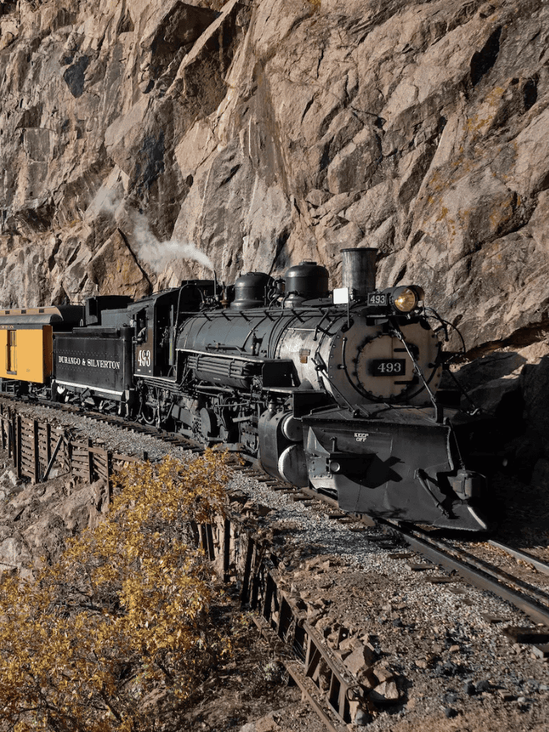Vintage steam locomotive traveling through rocky mountain landscape for scenic train rides.