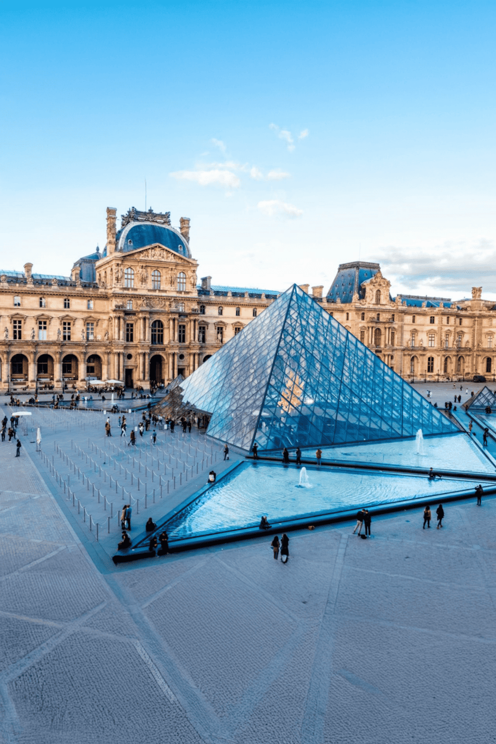 Modern glass pyramid at Louvre Museum in Paris, France, with historic architecture in the background.