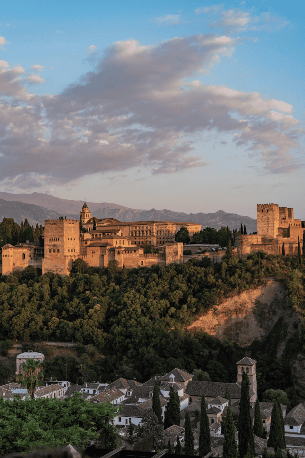 Ancient Alhambra Palace in Granada, Spain with scenic mountain backdrop at sunset.