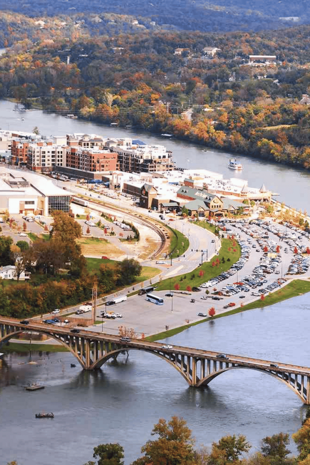 Vibrant cityscape along a winding river with bridges, buildings, fall foliage, and urban infrastructure.