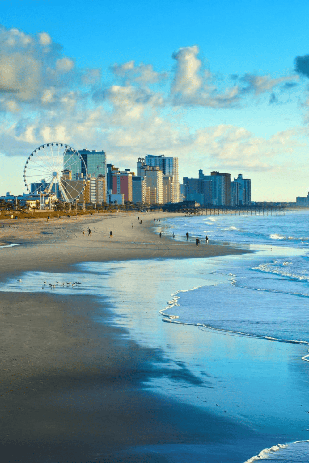Vibrant oceanfront skyline with Ferris wheel and sandy beach in sunny coastal city.