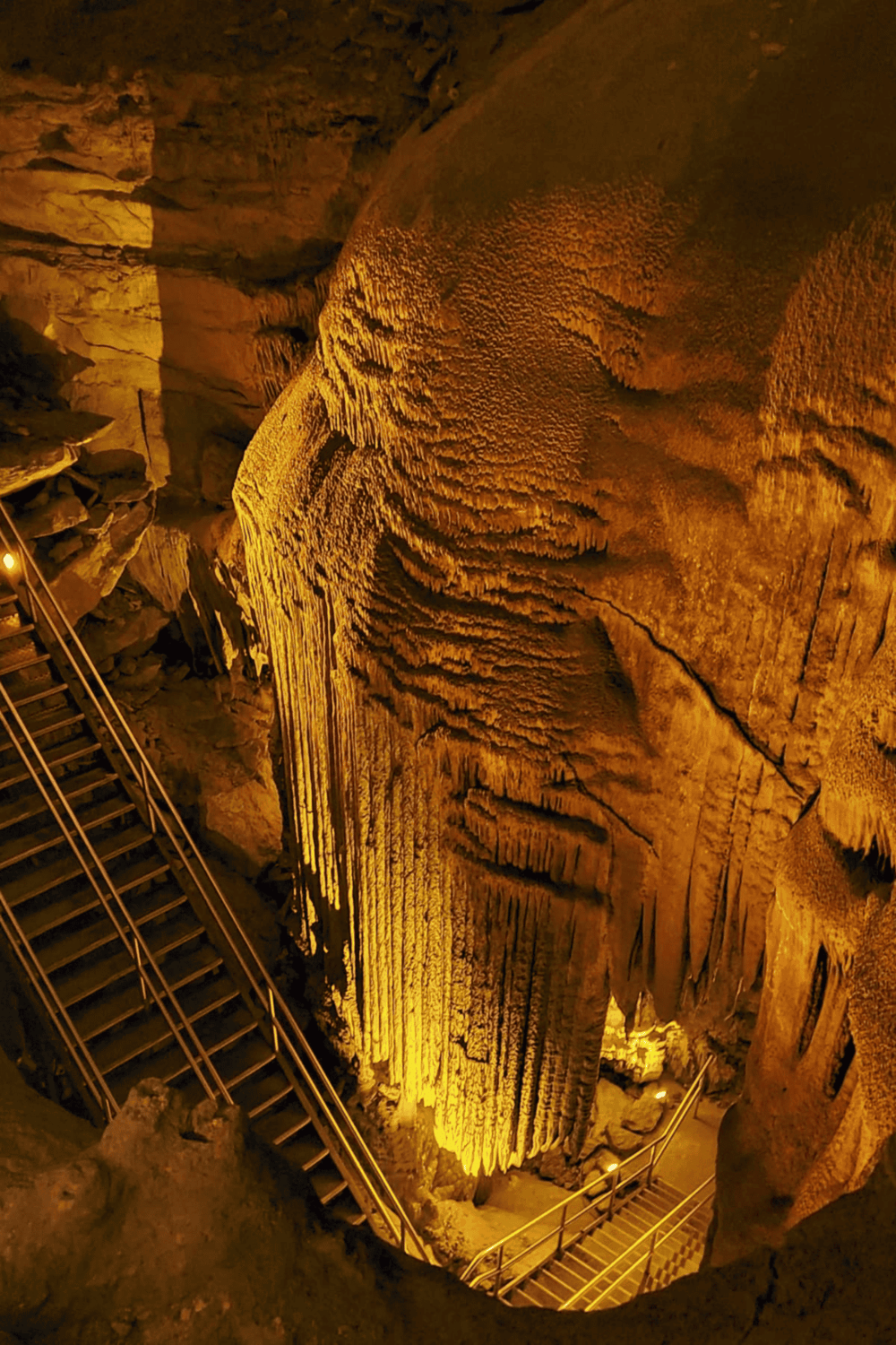 Stalactites and stalagmites in a illuminated cave, guiding visitors with pathways.