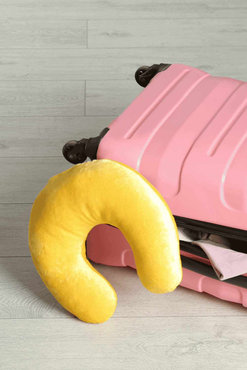 Pink suitcase with travel pillow on wooden floor | QuestForDirections travel essentials.