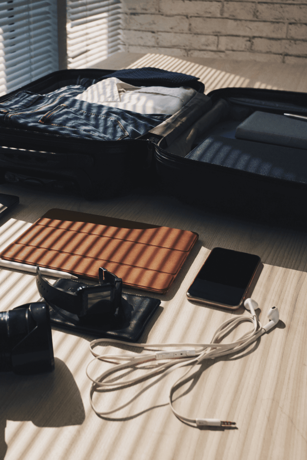 Dirty clothes in suitcase for travel packing, travel essentials on desk.