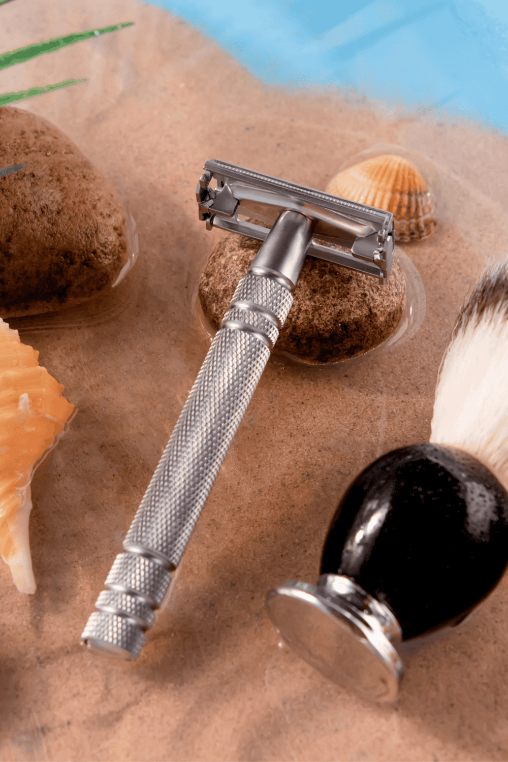 Razors, shells, and stones on sand beach with water.