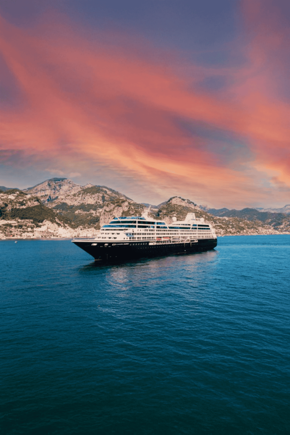 Luxury cruise ship sailing in Mediterranean sea at sunset, scenic coastal mountains.
