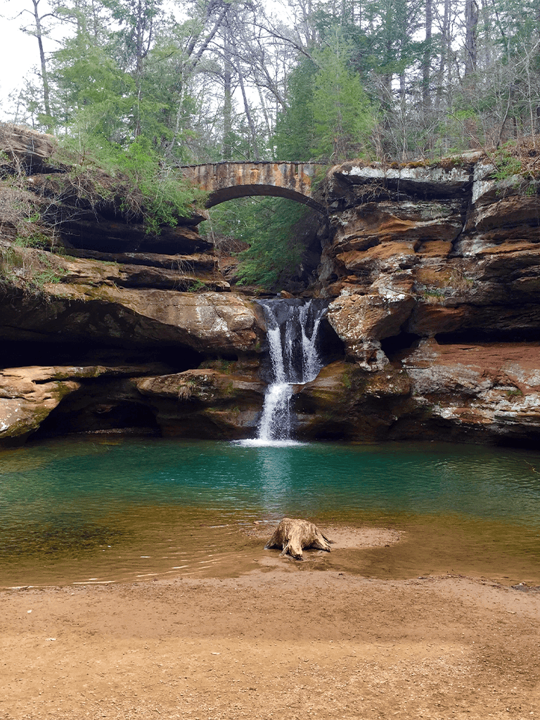 Serene waterfall cascading under a stone bridge in a lush forest setting.