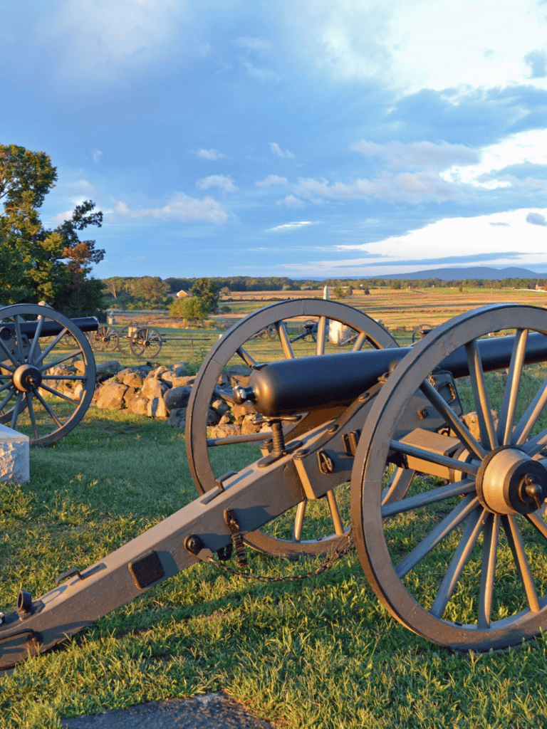 Ancient cannons on a historic battlefield under a blue sky with clouds, scenic outdoor military display.